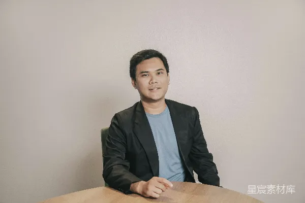 高清摄影 穿着黑色西装的男子坐在棕色木桌旁。