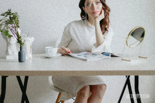 高清摄影 一位女士坐在桌子旁，手里拿着一本书，旁边放着一杯咖啡。
