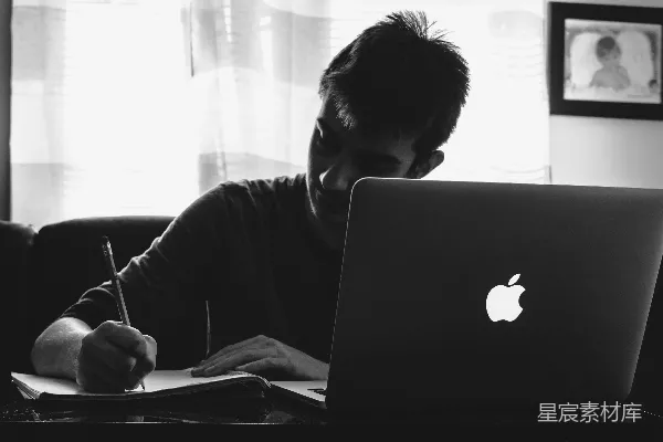 高清摄影 黑白色调的摄影作品，展示了一位男人在MacBook前写字的场景。