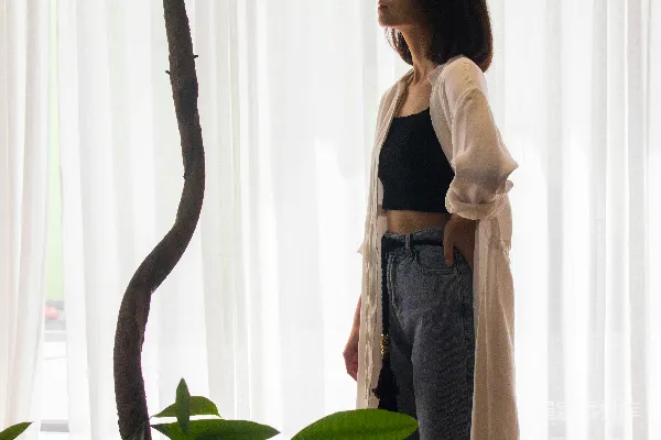 高清摄影 穿着黑色背心和蓝色牛仔裤的女人站在白色窗帘旁边。