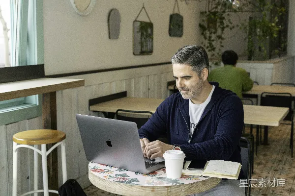 高清摄影 穿着蓝色毛衣的男人坐在桌子旁使用MacBook。