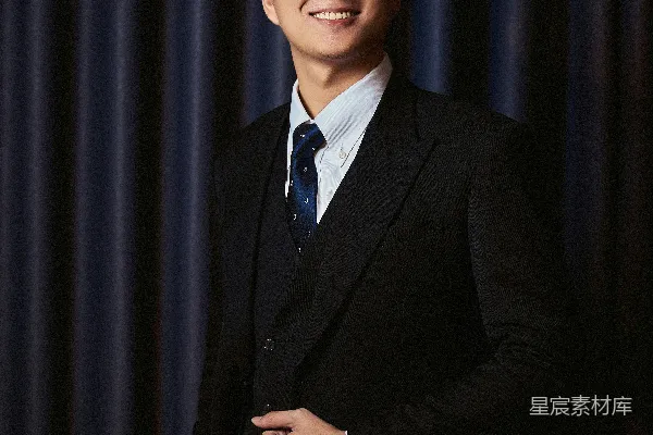 高清摄影 一位穿着西装、面带微笑的男人站在暗色的幕布前。