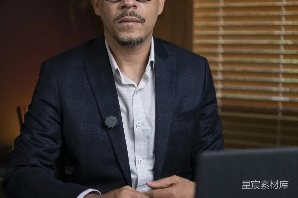 高清摄影 穿着西装的男人坐在办公桌前，面前放着笔记本电脑和手机。