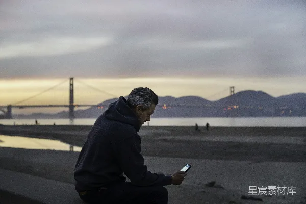 高清摄影 一个穿着黑色连帽衫的男人坐在白天的灰色混凝土人行道上。