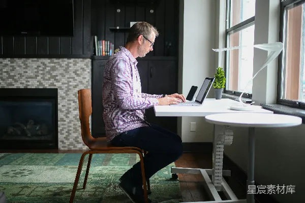 高清摄影 穿着灰色衬衫的男人坐在棕色木椅上使用MacBook Pro。