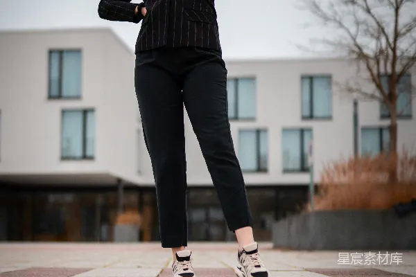 高清摄影 一个穿着黑色裤子和白色运动鞋的女人站在白天的灰色混凝土路面上。