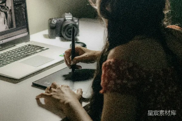 高清摄影 一位女性坐在桌子旁，面前有一台笔记本电脑和一台摄像机。