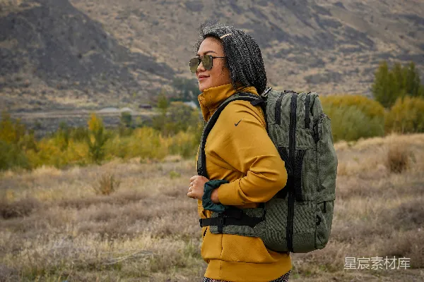 高清摄影 一个穿着黑白格子裙、背着黑色背包的女人站在绿草地上。
