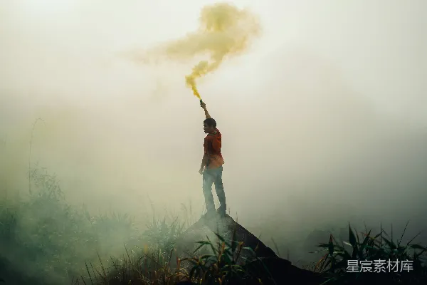 高清摄影 一个站在岩石形成的男人拿着黄色的信号弹，周围是雾气。