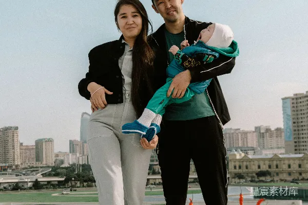 高清摄影 带着婴儿的家庭在户外摆姿势，背景是城市景观。