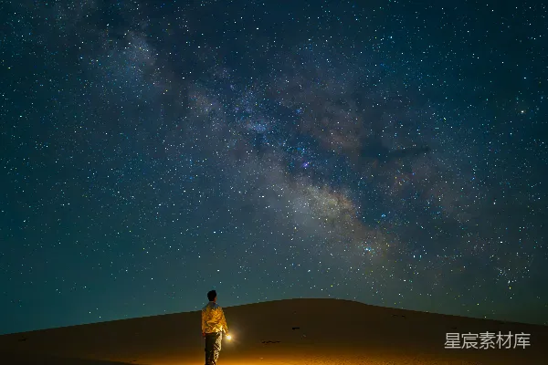 高清摄影 一个男人站在一个沙丘顶部，头顶上是充满星星的夜空。