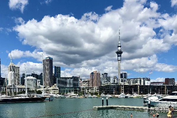 高清摄影 在城市建筑旁的水面上，有一艘黑白相间的船，天空中有蓝色和白色的云朵，天气晴朗。