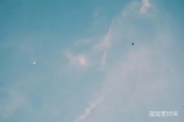 高清摄影 一架飞机在空中飞行，背景中有半轮明月。