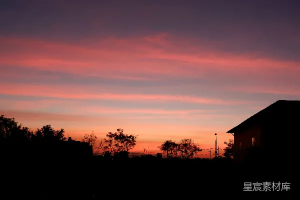 高清摄影 夕阳西下，天空色彩斑斓，树木剪影与房屋交织。