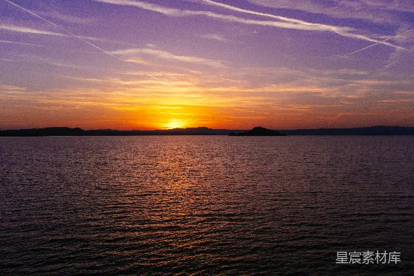 高清摄影 夕阳映照在水面上，天空中有飞机尾迹。