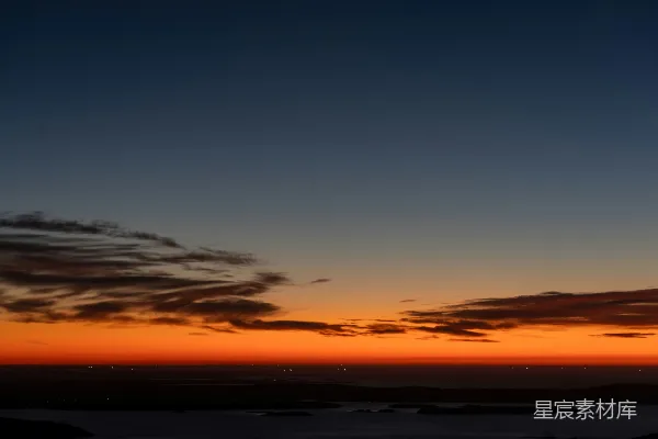 高清摄影 夕阳照耀在平静的海洋上，远处的灯光闪烁。