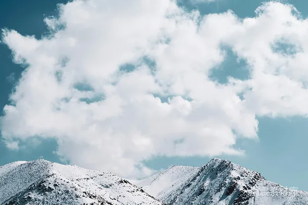 高清摄影 一座覆盖着积雪的山峰在多云的蓝天之下