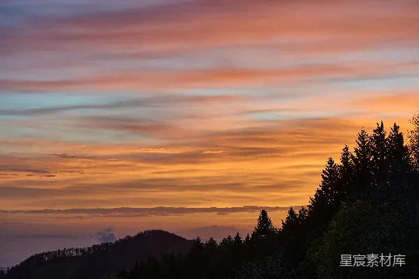 高清摄影 彩霞满天的夕阳映照着剪影的树木和山丘。