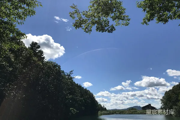 高清摄影 白天，河边绿树成荫，天空湛蓝，白云飘浮。