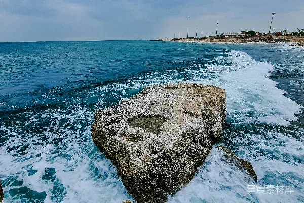 高清摄影 一块大石头坐落在海滩上，旁边是海洋。