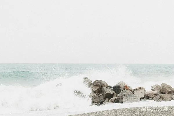 高清摄影 灰白色的海滩上，海浪拍打着岩石。
