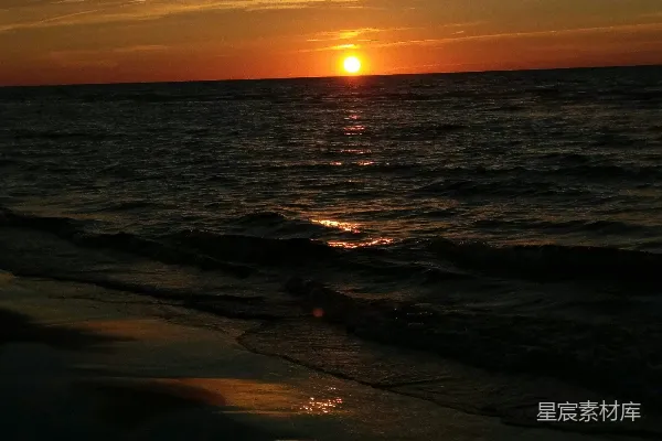 高清摄影 夕阳正缓缓落下，映照在海滩上的水面上。
