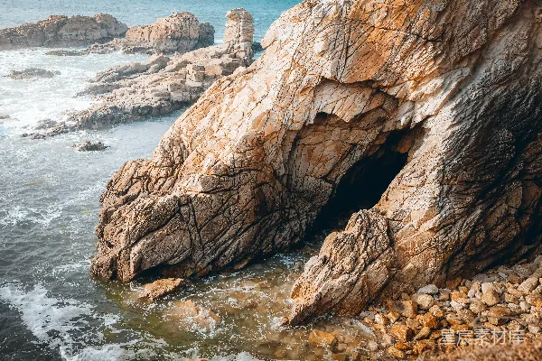 高清摄影 一座巨大的岩石形成坐落在海滩上，旁边是海洋。