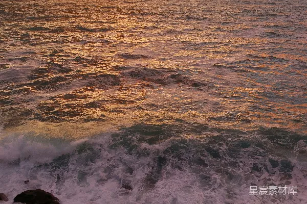 高清摄影 夕阳正缓缓落下，海面波光粼粼，前景中岩石隐约可见。