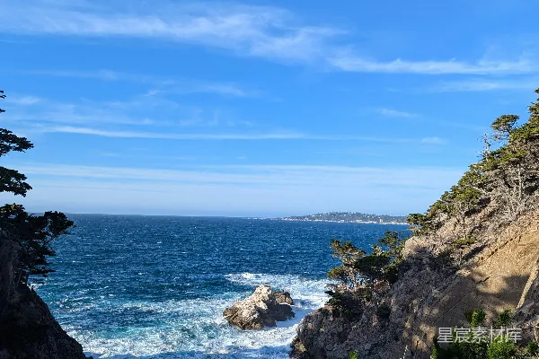高清摄影 波浪在晴朗的蓝天背景下拍打着岩石海岸线。