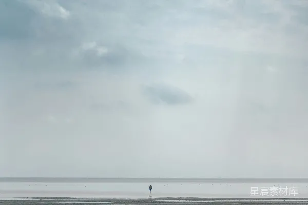 高清摄影 一个孤独的人站在远处的海滩上。