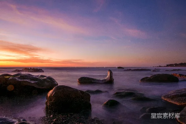 高清摄影 夕阳正在海洋上落下，前景中可以看到岩石。