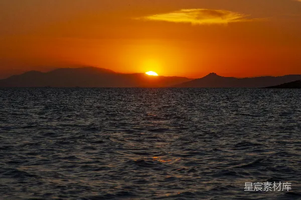 高清摄影 夕阳正挂在海洋上空，远处的山脉若隐若现。