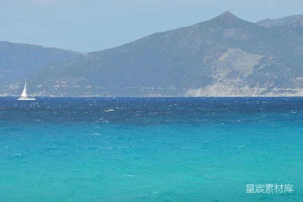 高清摄影 在蓝色的大海上，一艘帆船在远处的山峦前航行。