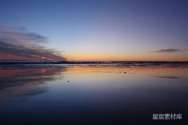 高清摄影 夕阳正缓缓落下，洒落在海面上，天空的颜色倒映在波光粼粼的水面上。