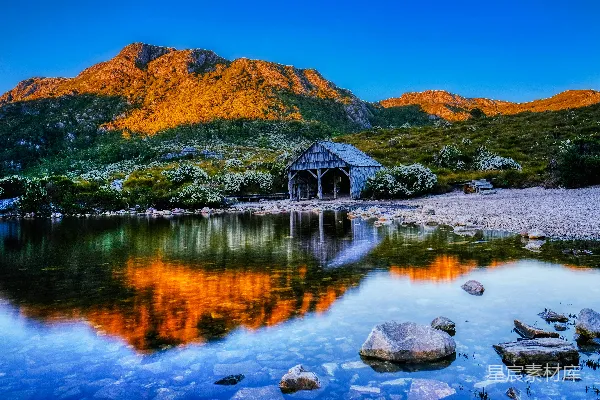 高清摄影 湖边棕色的木屋在蓝天下的白天，旁边是棕色的山。