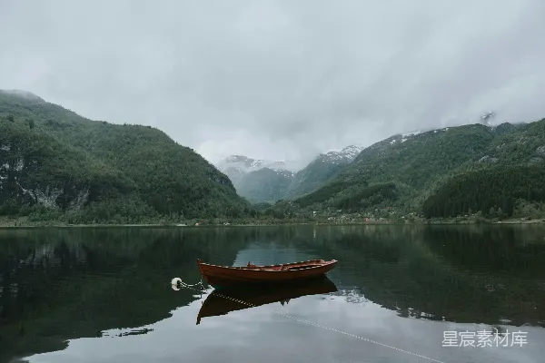 高清摄影 白天，棕黄色的小船停泊在靠近绿山的水面上，天空万里无云。