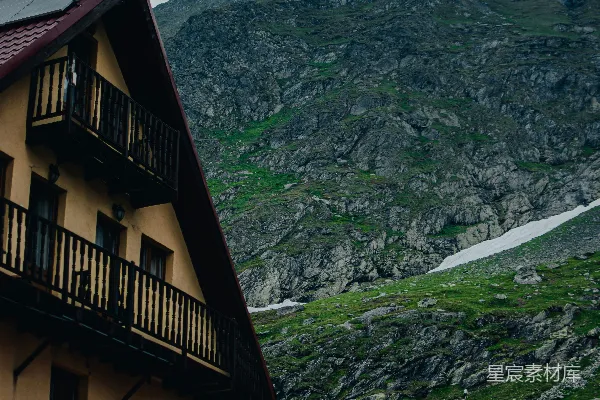 高清摄影 一座质朴的山间小屋矗立在布满雪迹的岩石山峰前。