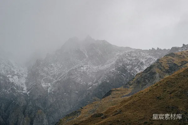 高清摄影 雾气缭绕的雪山峰顶，覆盖着积雪和干草。