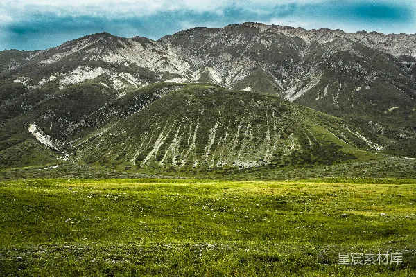 高清摄影 白天的雪山上有一片绿色的草地。