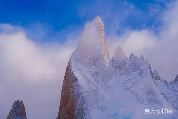 高清摄影 一座被白雪和云层覆盖的山峰在蓝天之下