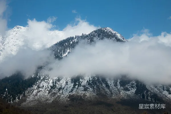 高清摄影 一座覆盖着积雪和云雾的山在蓝天之下