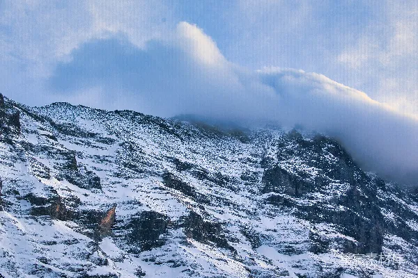高清摄影 一座被积雪和云雾覆盖的山峰，在蓝天的映衬下。