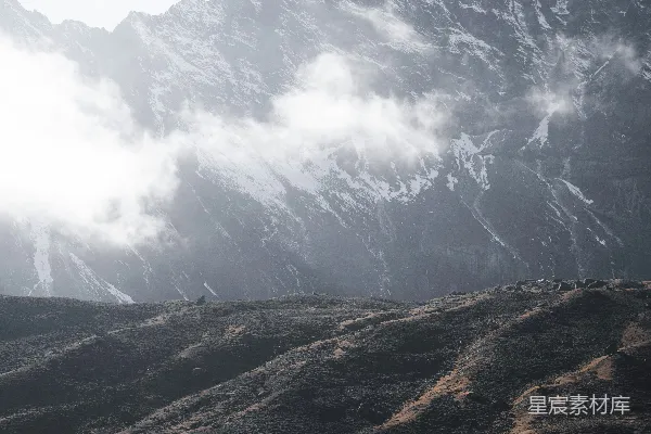 高清摄影 雾气缭绕的雪山，高耸于干燥的岩石丘陵之上。
