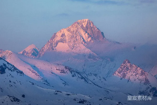 高清摄影 雪山峰顶被柔和的粉红色日出光线照亮。