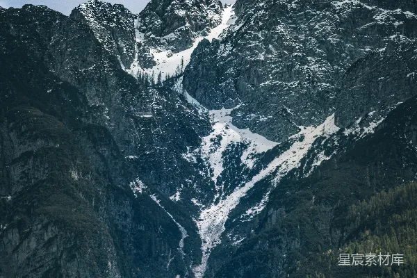 高清摄影 白雪皑皑的山峰在多云的天空下衬着绿树。