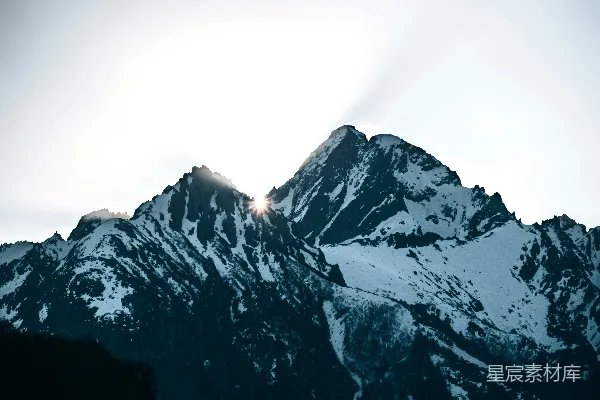 高清摄影 被雪覆盖的山峰，阳光透过云层照耀。
