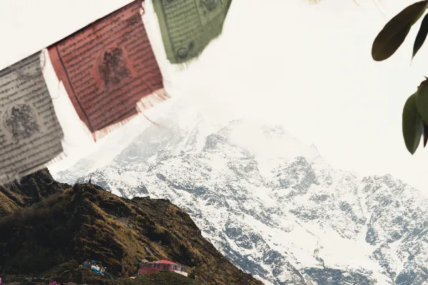 高清摄影 五彩缤纷的经幡飘扬在雪山脚下的小木屋上空，远处是积雪覆盖的山峰。