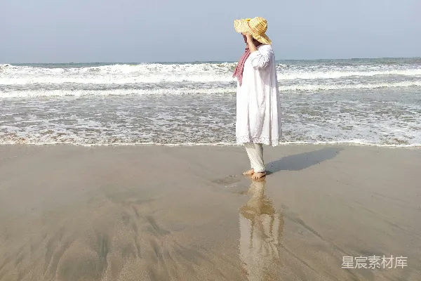 高清摄影 白天，一位穿着白色连衣裙的女士站在海滩上。