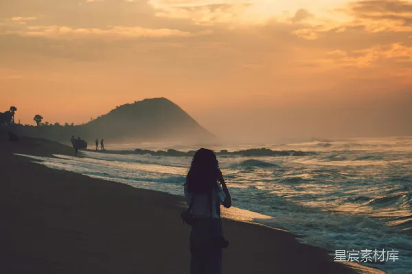 高清摄影 一个穿着黑色夹克的女人站在海边，夕阳西下。