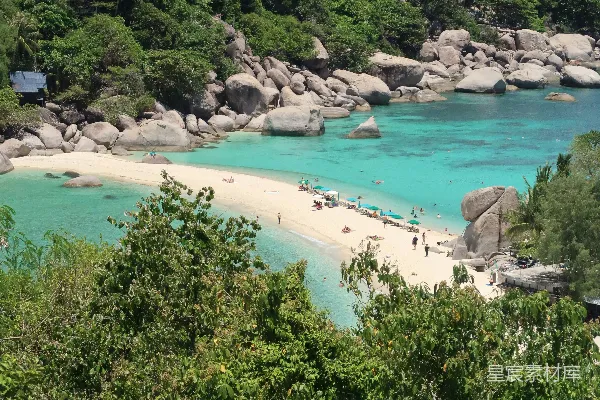 高清摄影 一片沙滩，被绿色的树木和蓝色的海水包围着。